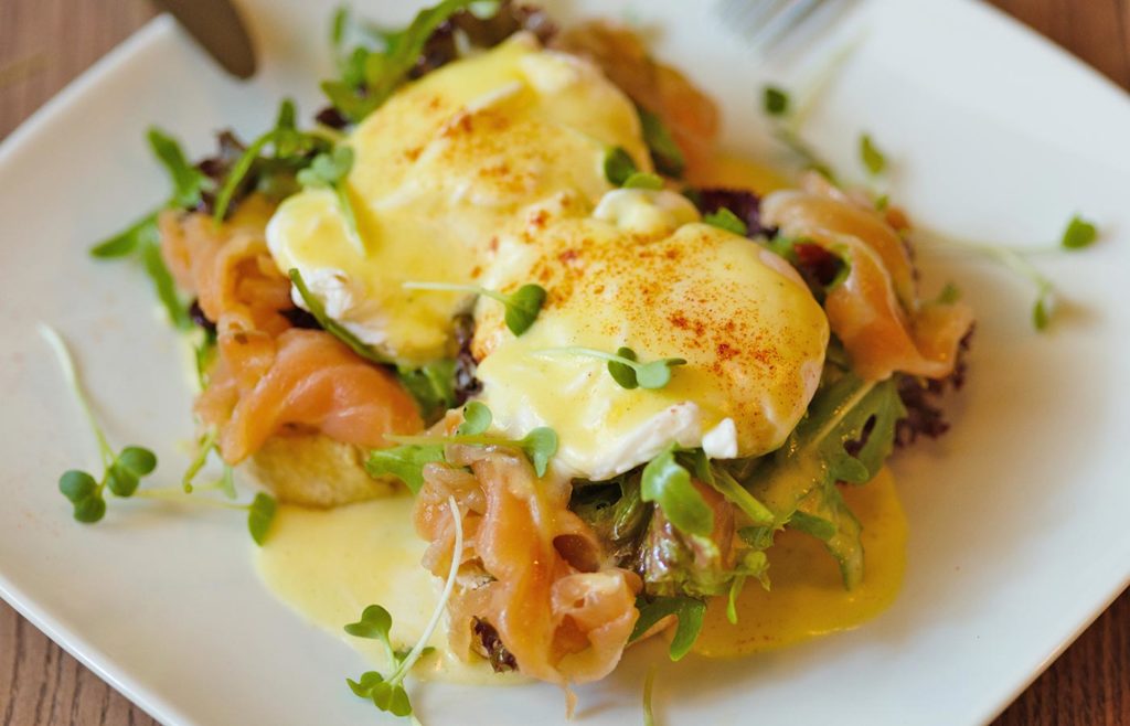 Eggs Benedict with smoked salmon, greens, and hollandaise sauce on a white plate.