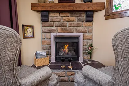A stone fireplace with a lit fire, two wine glasses on the hearth, and two armchairs facing it.