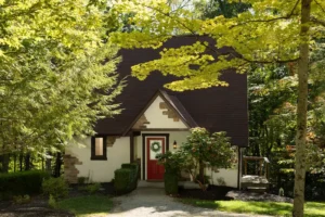 A Tudor-style home with a red front door and a dark roof, framed by green trees.